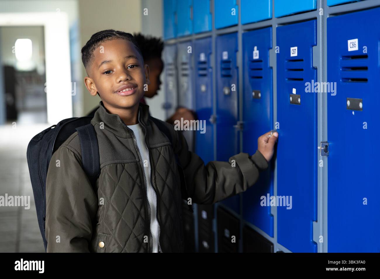 Apertura dell'armadietto nel corridoio della scuola, ragazzo sorridente e con zaino Foto Stock