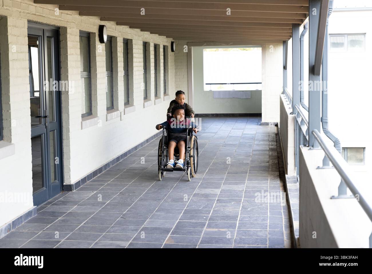 Ragazzi diversi nel corridoio della scuola, un amico che spinge in sedia a rotelle, si diverte insieme Foto Stock