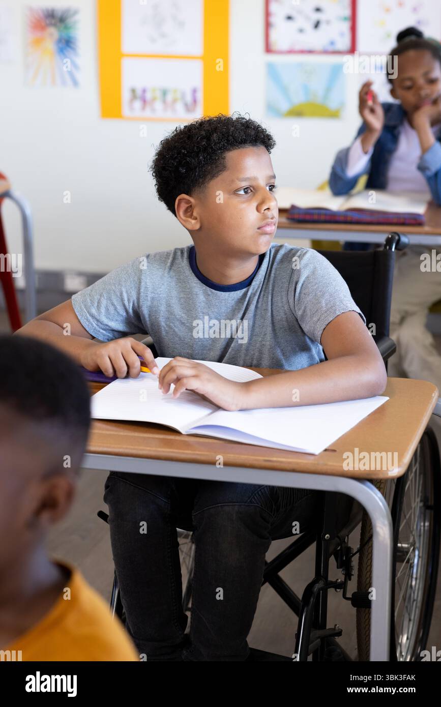 In classe, ragazzo in sedia a rotelle ascoltando attentamente durante la lezione scolastica Foto Stock