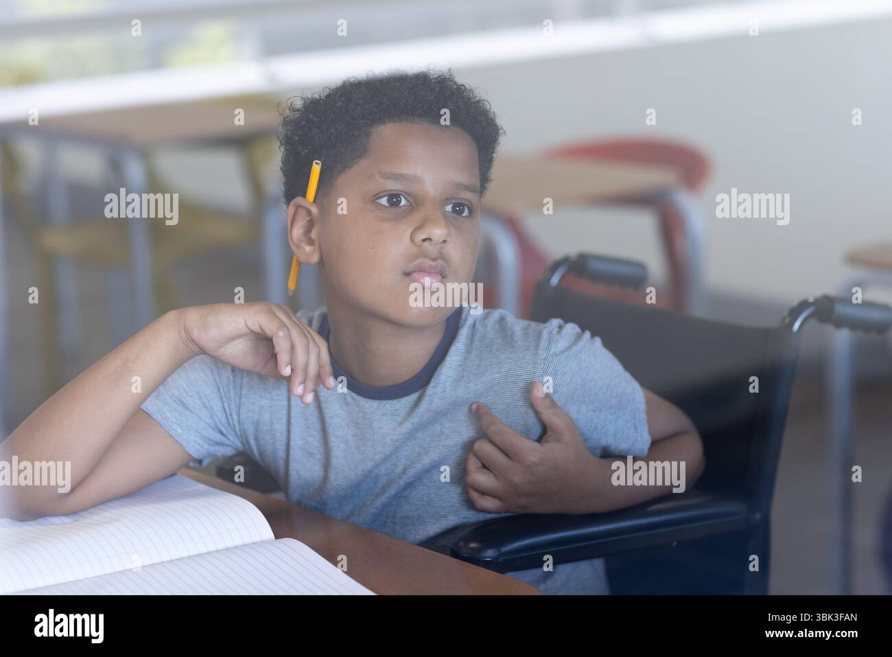 Ragazzo in sedia a rotelle che ascolta attentamente in classe con un notebook aperto, a scuola Foto Stock