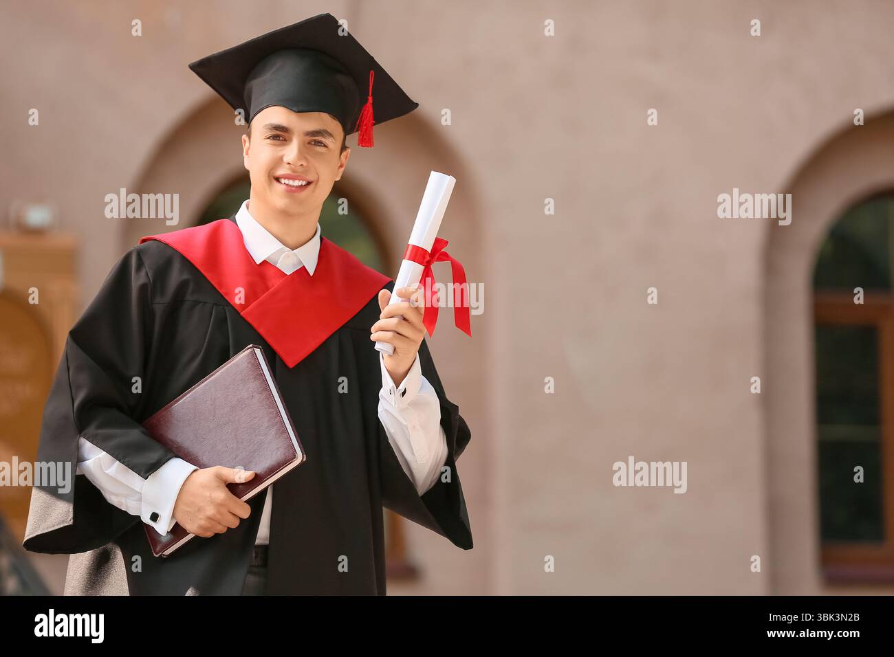 Felice studente di sesso maschile con diploma e libro il giorno della sua laurea Foto Stock