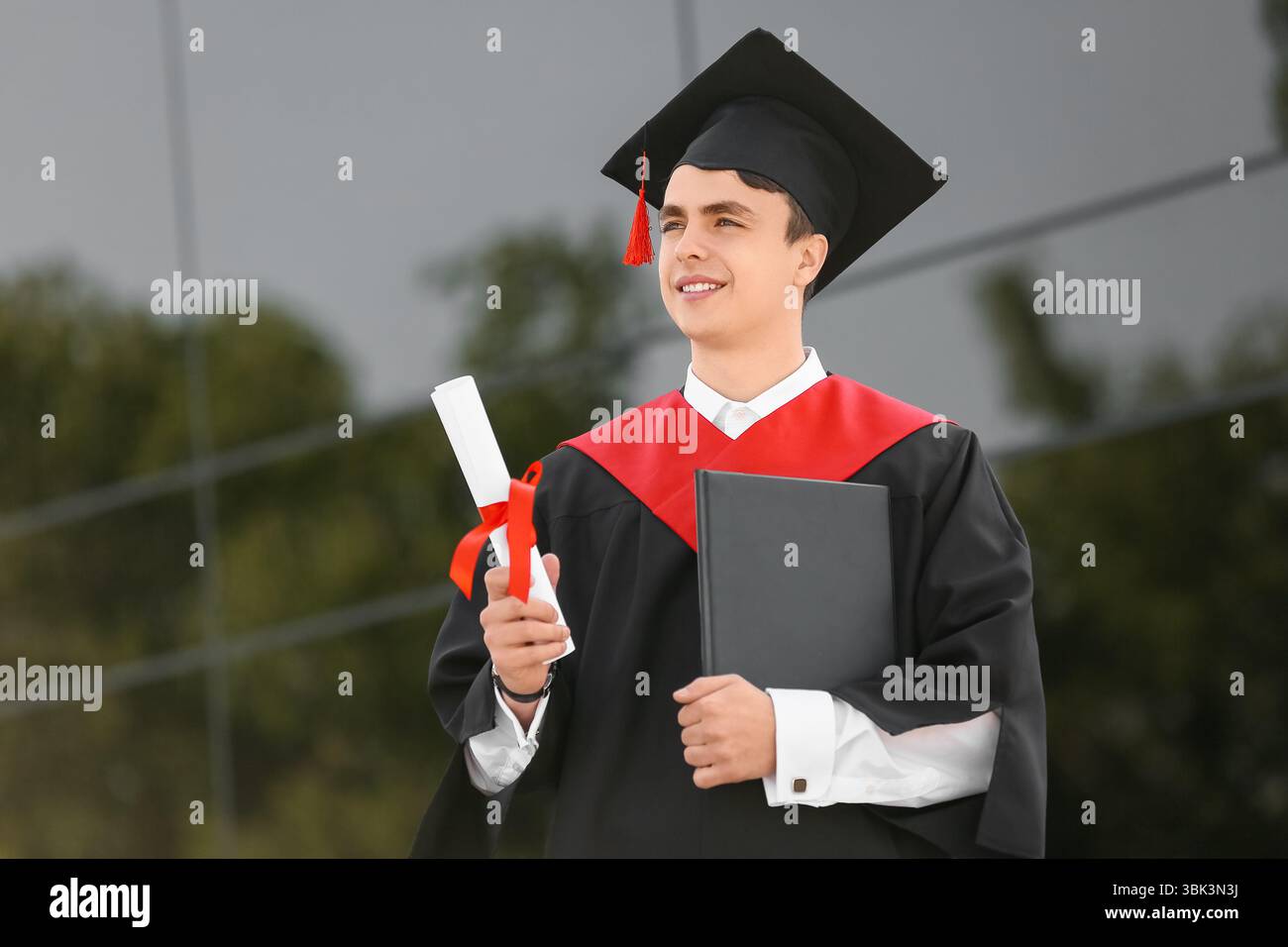 Studente laureato con diploma e libro vicino all'università Foto Stock