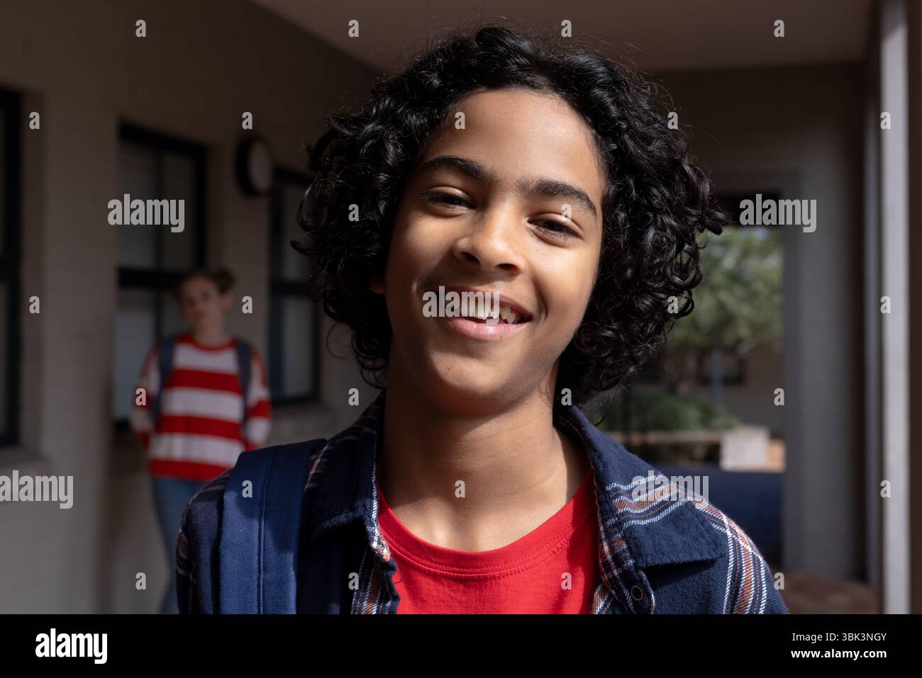 Ragazzo sorridente con zaino che si gode la giornata scolastica nel soleggiato corridoio all'aperto Foto Stock