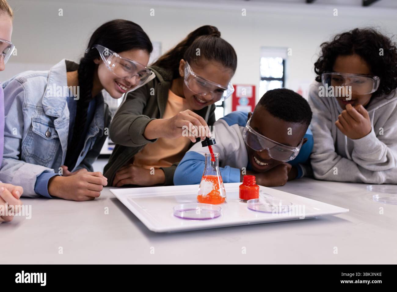 Diversi studenti in classe scientifica che sperimentano con il becher, indossando occhiali di sicurezza, a scuola Foto Stock