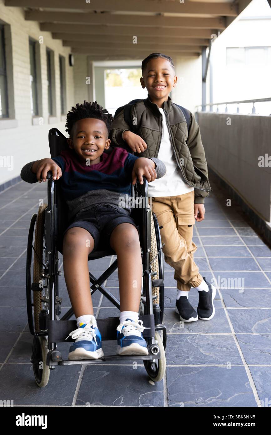 Sorridendo ragazzi diversi a scuola, ragazzo in sedia a rotelle con un compagno di classe di supporto Foto Stock