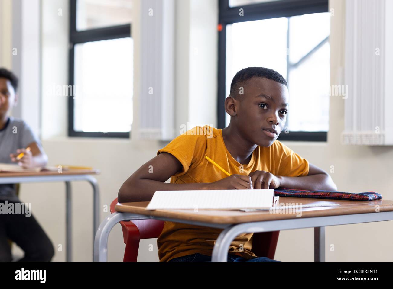 In classe, ragazzo afroamericano concentrato che scrive su un taccuino durante la lezione scolastica Foto Stock