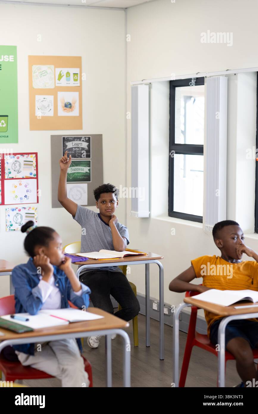 In classe, ragazzo che alza la mano mentre diversi studenti ascoltano attentamente l'insegnante, a scuola Foto Stock