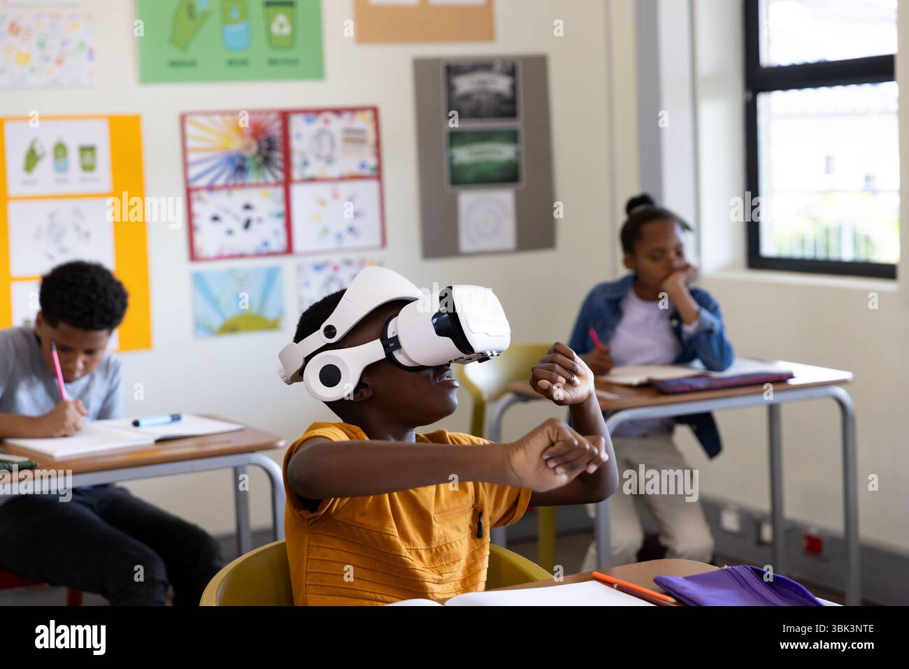In classe, ragazzo afroamericano che usa il visore VR mentre i compagni di classe studiano alla scrivania, a scuola Foto Stock
