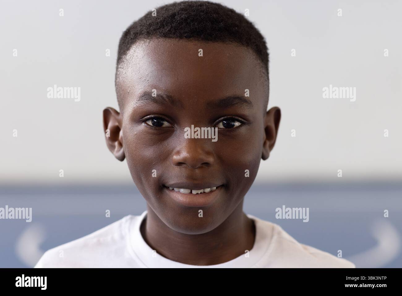 Sorridente ragazzo afroamericano in classe con camicia bianca, sentendosi sicuro di sé e felice Foto Stock