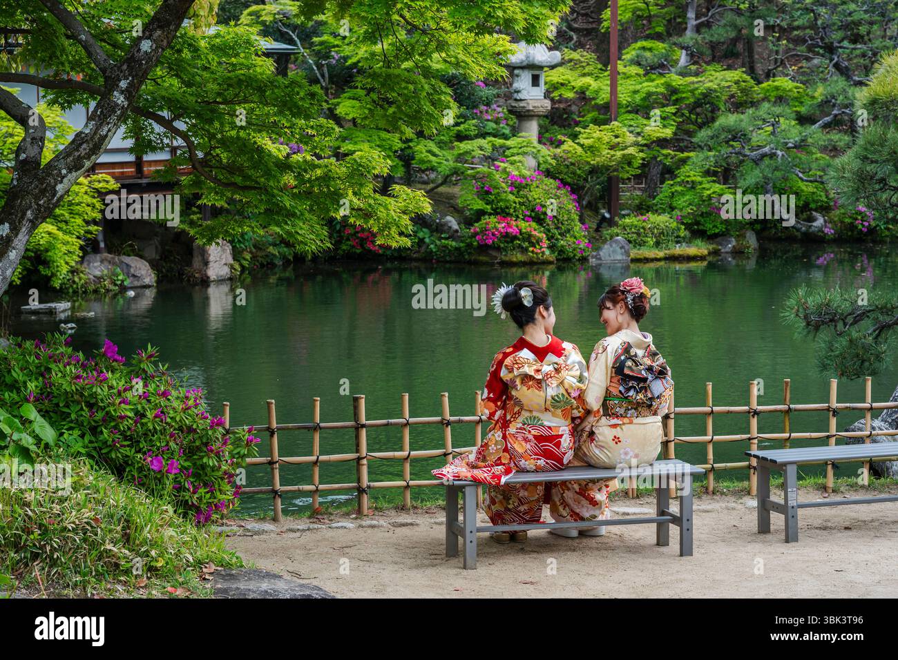 Due giovani donne giapponesi vestite di kimono, sedevano su una panchina a conversare. Giardini Sorakuen, Kobe, Giappone. Foto Stock