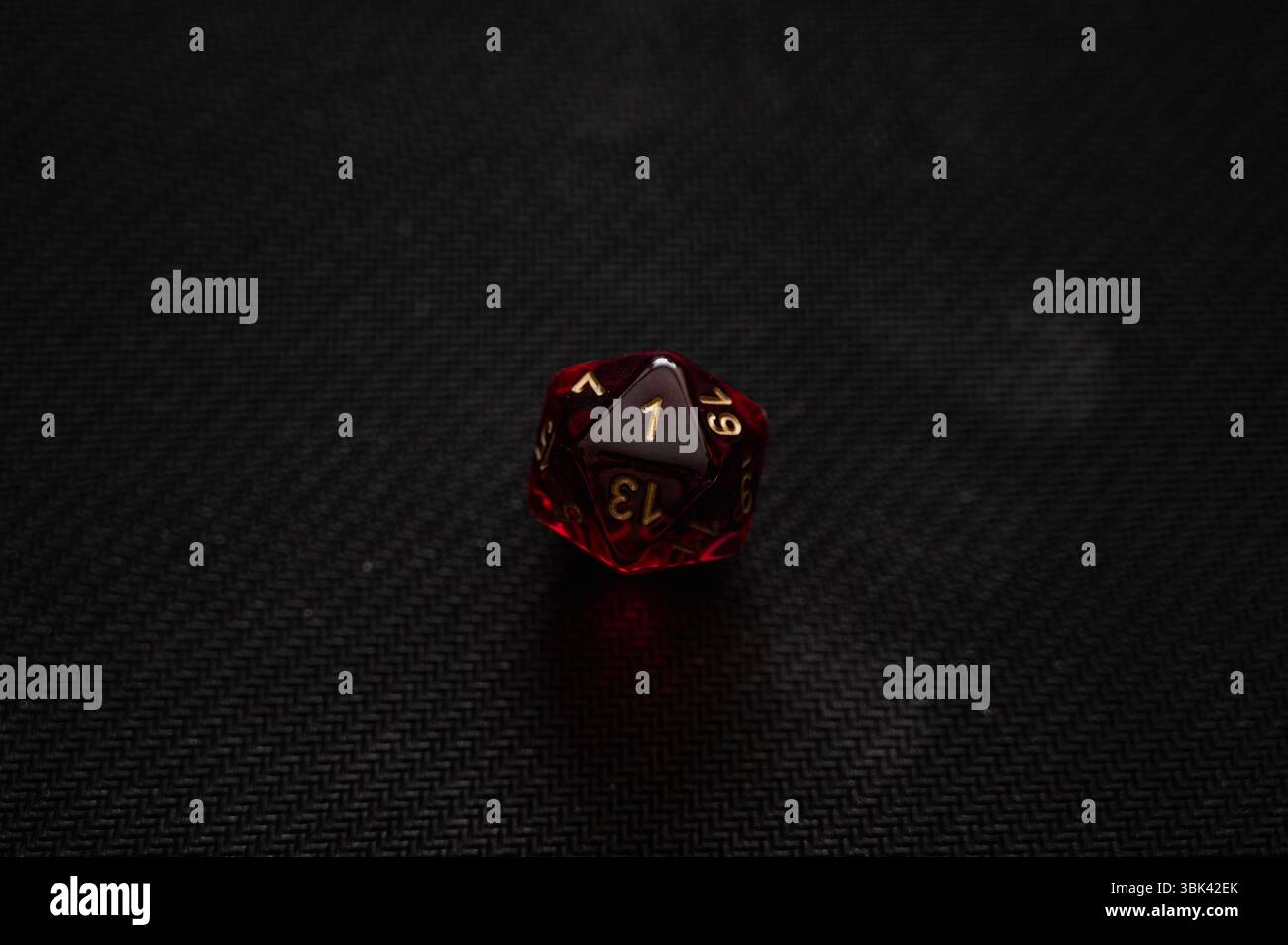Un'immagine macro drammatica di un singolo dado D20 rosso traslucido su sfondo nero, che mostra il numero "1". Questa immagine simboleggia un errore critico, Foto Stock
