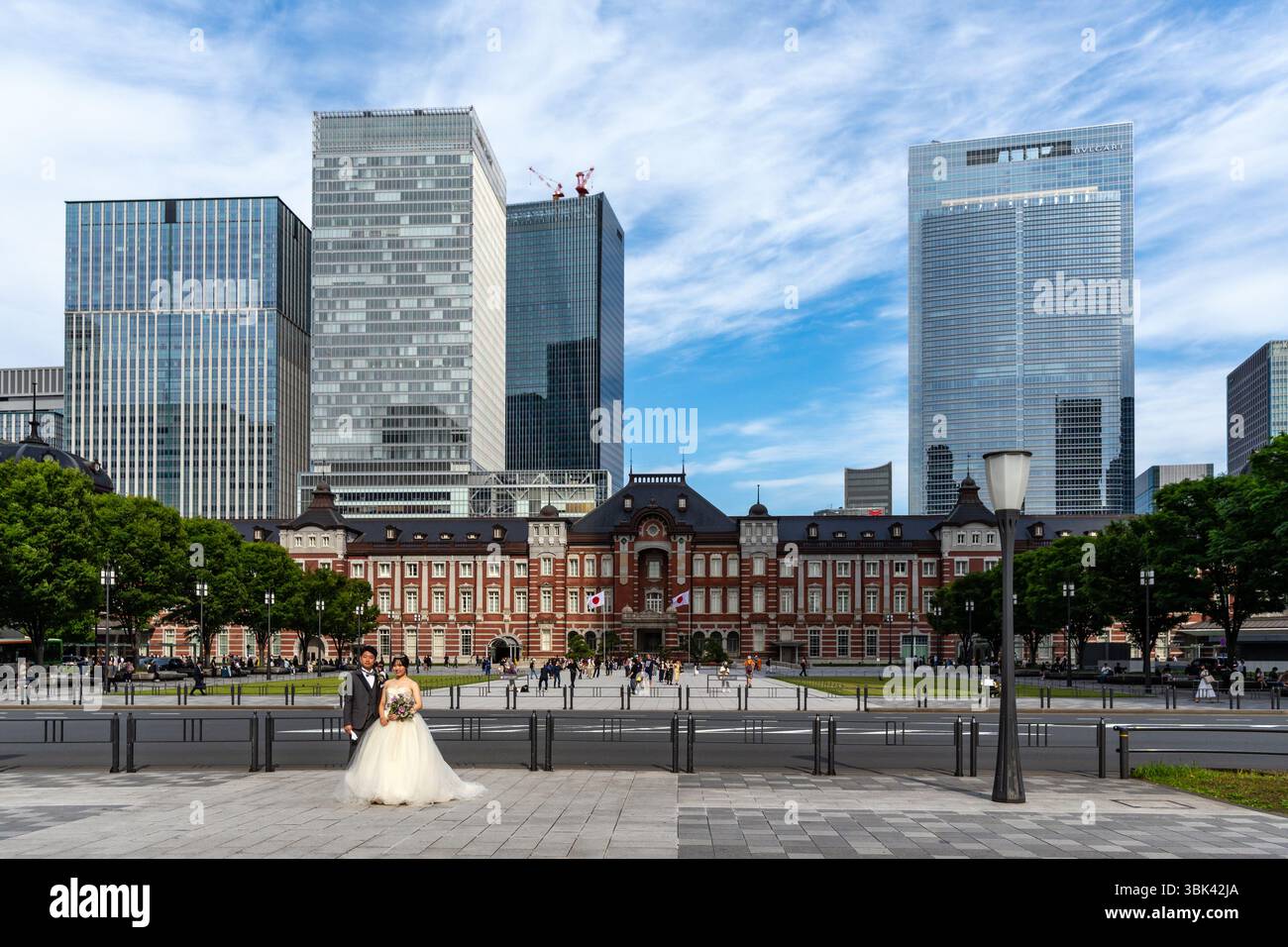Coppia in posa per foto di matrimonio in Piazza Marunouchi, con la stazione di Tokyo in mattoni rossi e gli alti edifici alle spalle. Foto Stock