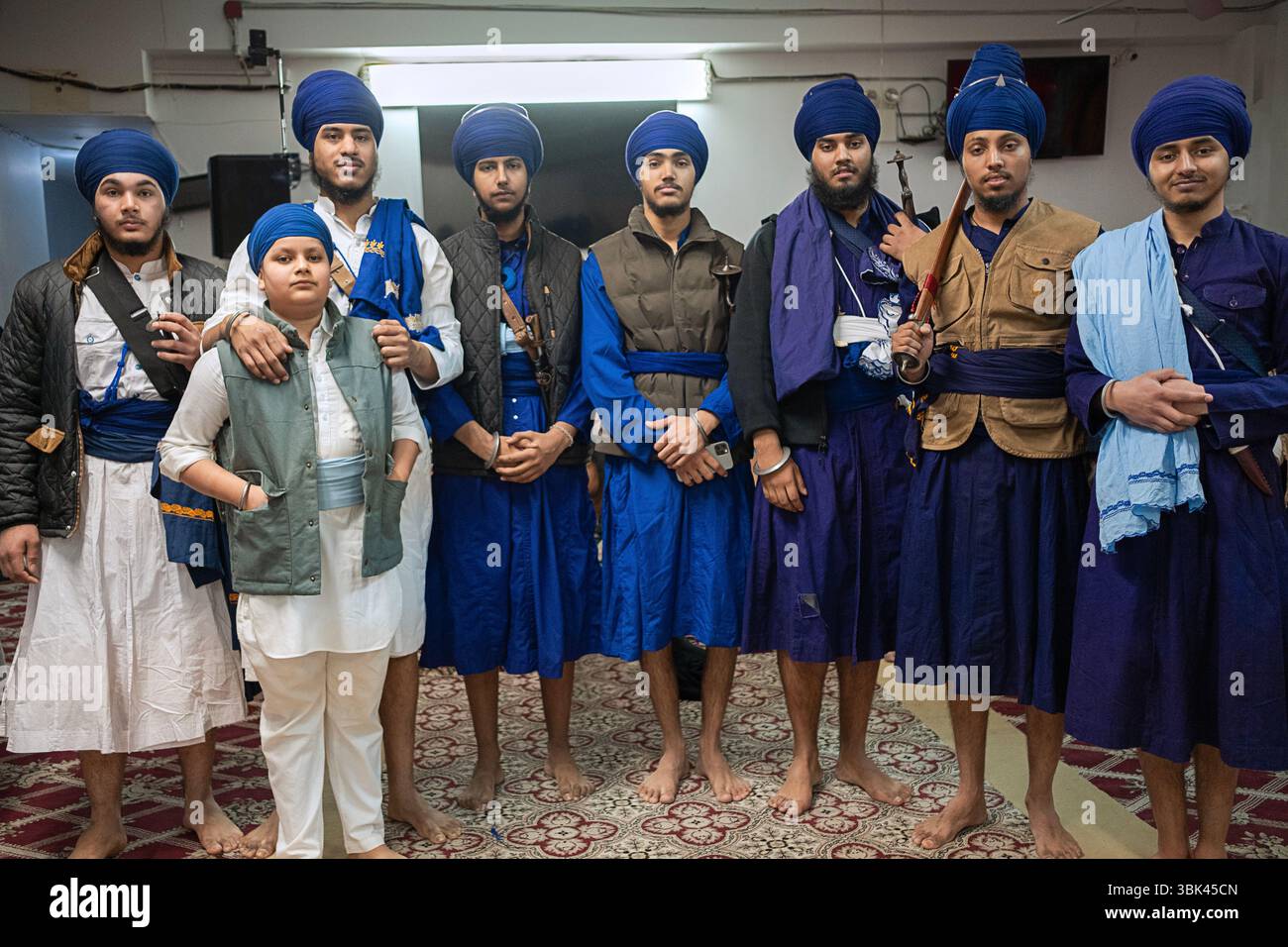 8 ragazzi attendono l'inizio di Gatka, un tradizionale concorso di arti marziali religiose in un tempio a South Richmond Hill, Queens, New York. Foto Stock