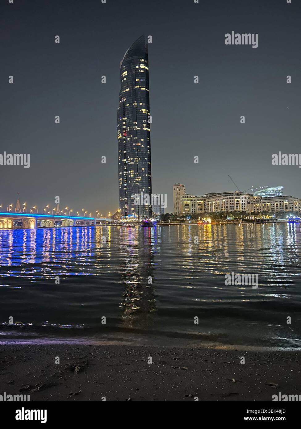 Vista notturna sul lungomare di Dubai con un ponte sulla sinistra e l'illuminato Versace Hotel e la D1 Tower sull'acqua Foto Stock
