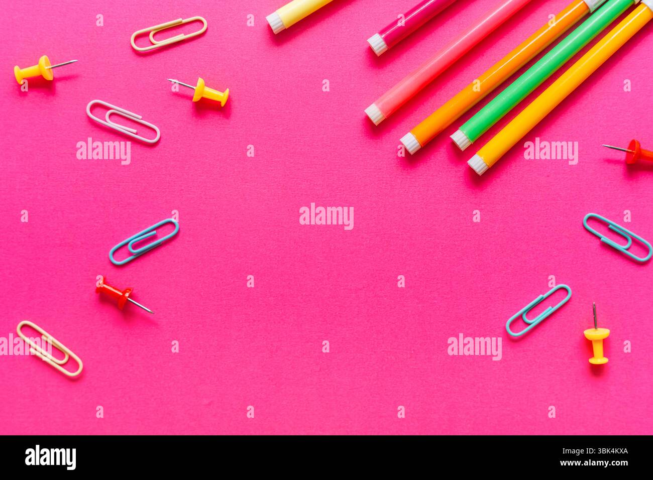 Penne colorate, graffette e perni a pressione disposti su uno sfondo rosa brillante. Concetto di ritorno a scuola in stile pop art. Foto Stock