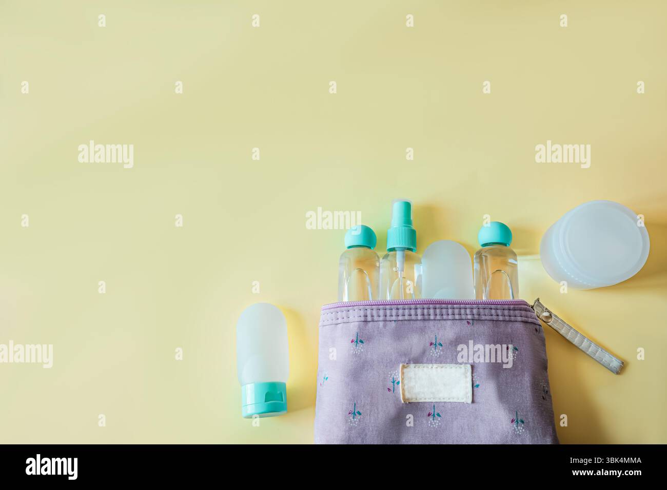 Piatto di una borsa viola da bagno riempita di bottiglie cosmetiche da viaggio su un morbido sfondo giallo. Accessori da viaggio dal design minimalista e femminile Foto Stock