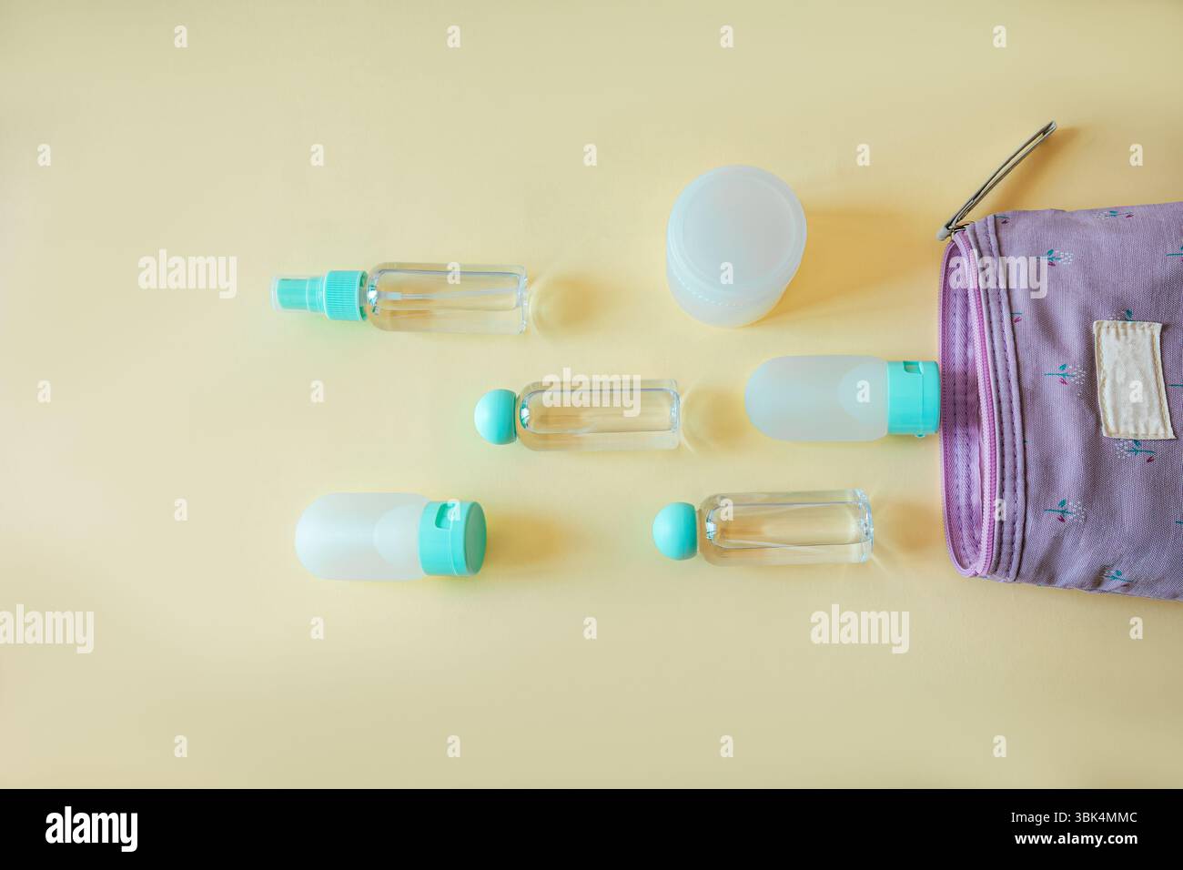 Piatto e minimalista di bottiglie da viaggio assortite e vasetti da bagno con una pochette cosmetica alla lavanda su un morbido sfondo giallo. Ideale per i viaggi, bello Foto Stock