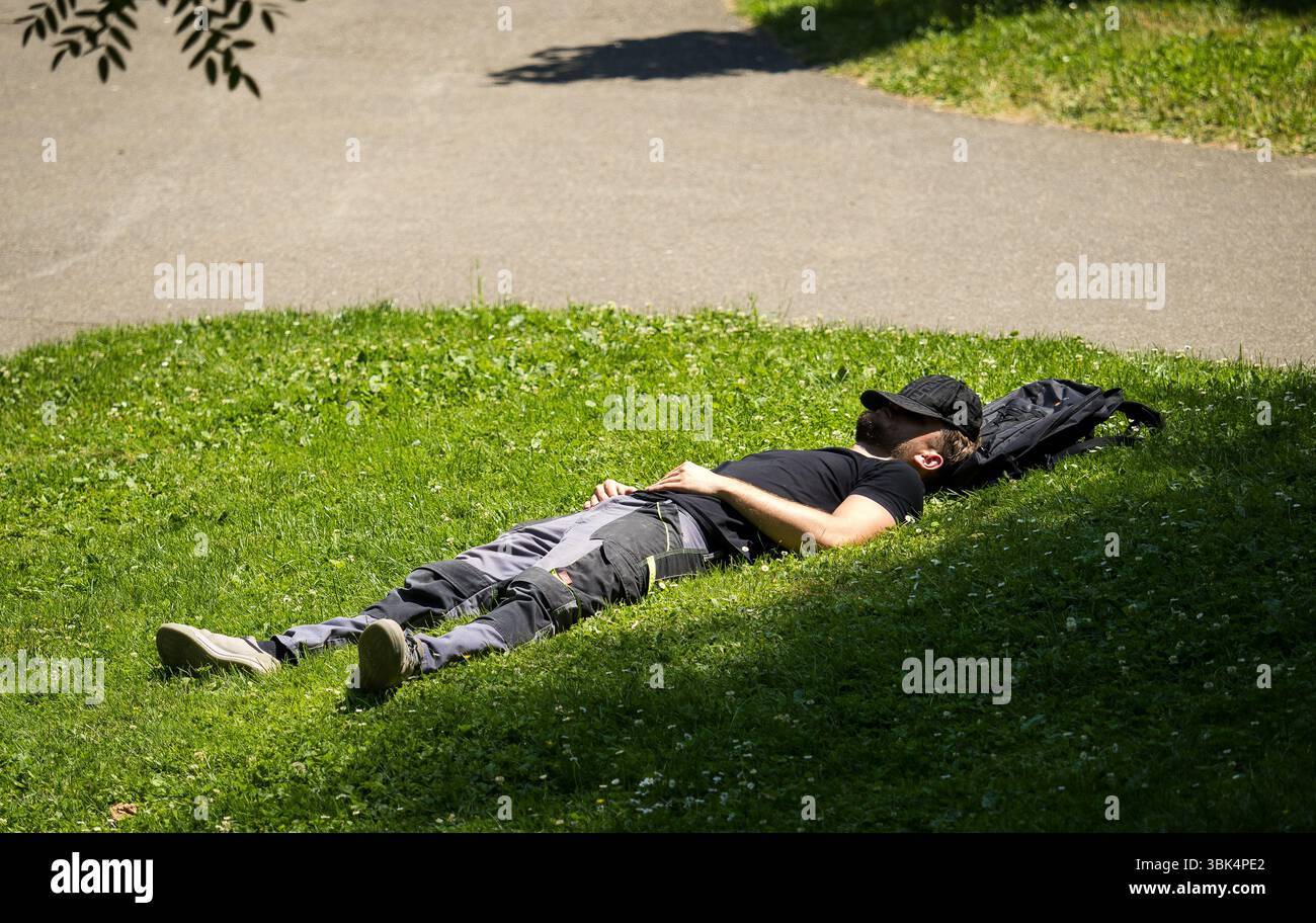 Ginevra, Svizzera. Giugno 2025. Una persona giace sull'erba in un parco cittadino, in cerca di riposo sotto il sole estivo, mentre un'ondata di caldo porta temperature insolitamente alte a Ginevra e in altre parti della Svizzera e dell'Europa. Crediti: Freddie Yeo / Alamy Live News Foto Stock