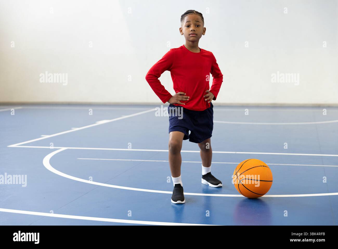 Ragazzo sicuro di sé in palestra in piedi con il pallacanestro sul campo al coperto Foto Stock