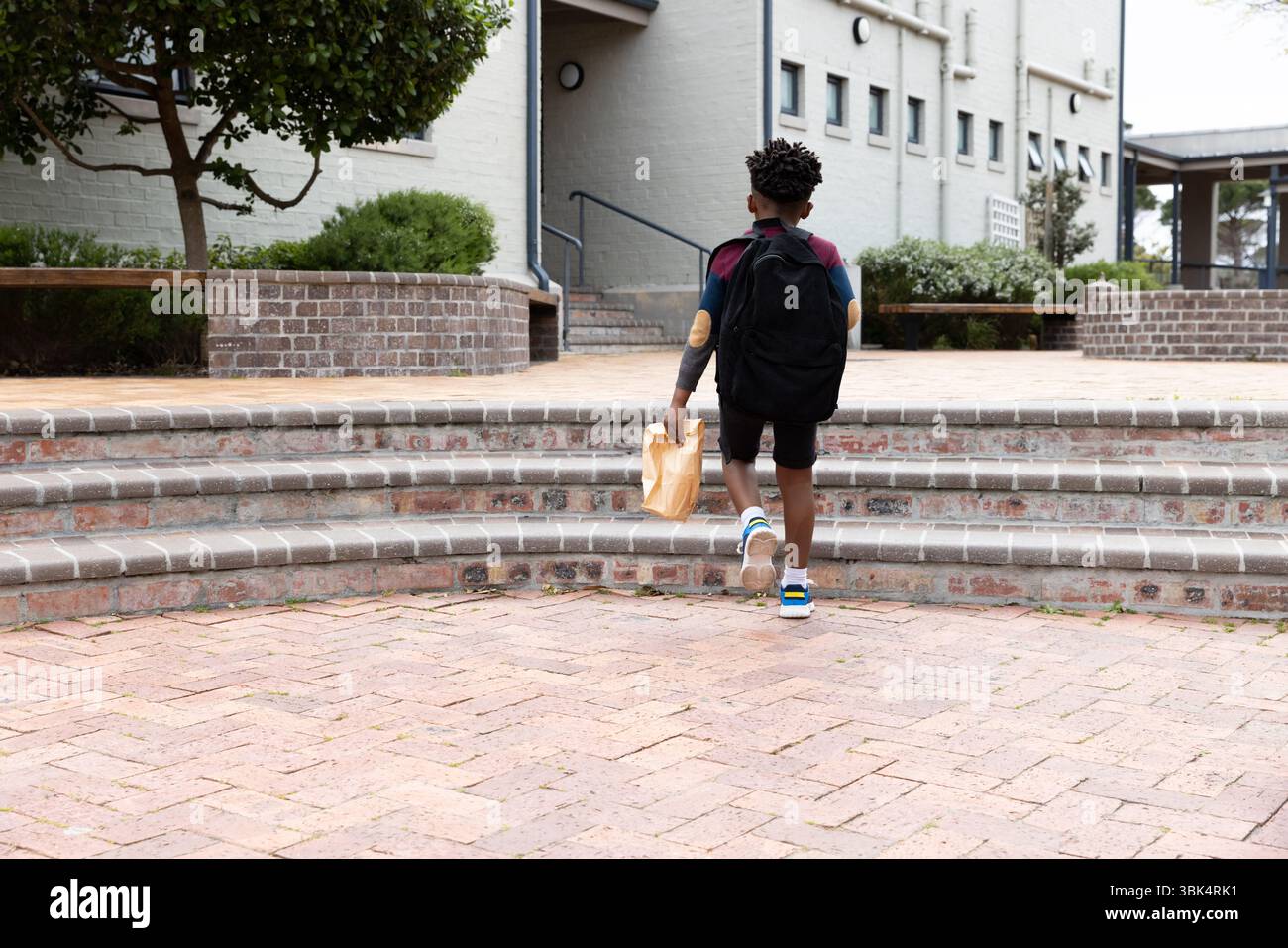 Ragazzo afroamericano con zaino che sale i gradini della scuola tenendo in mano il cestino per il pranzo Foto Stock