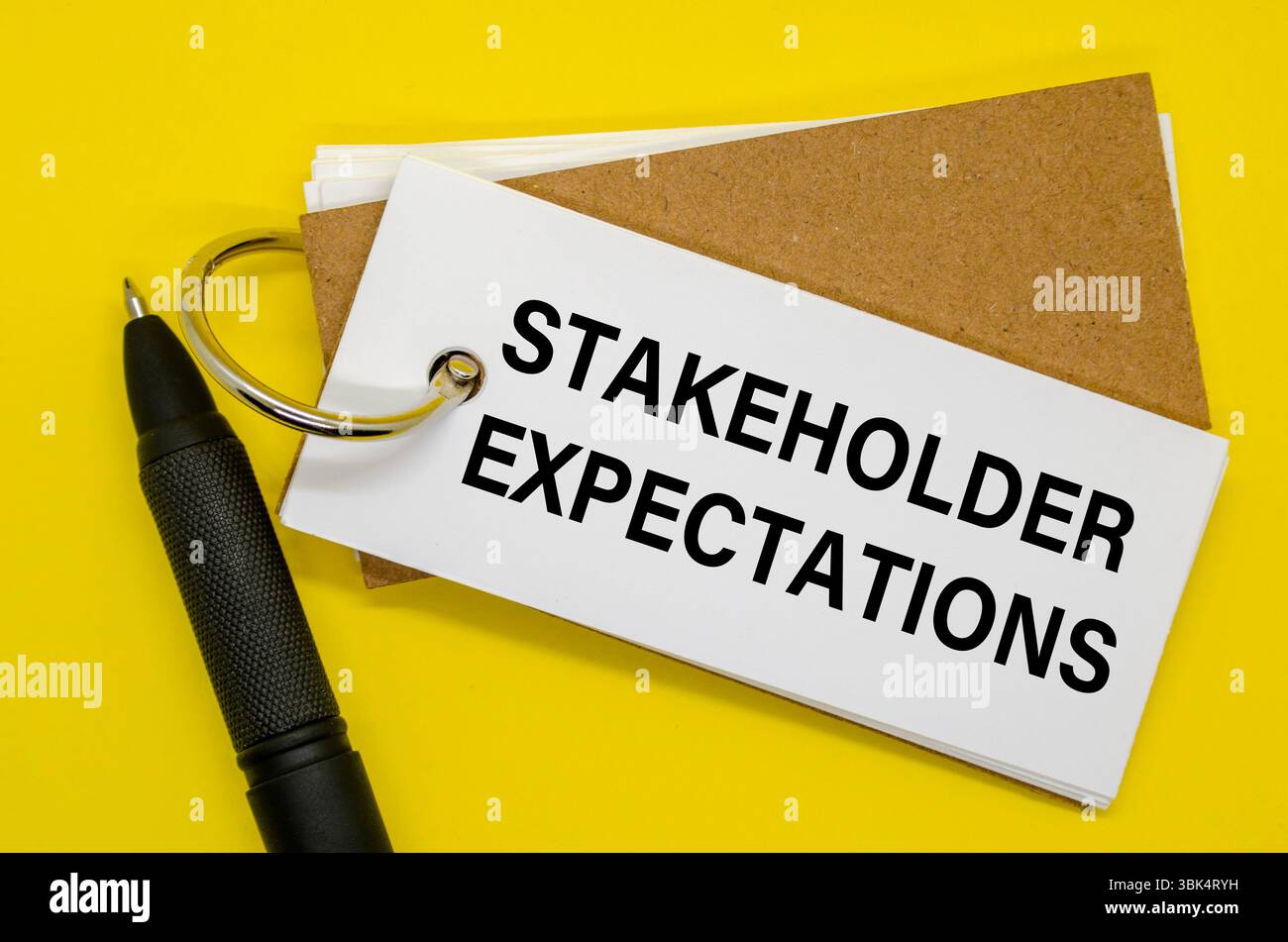 Notebook di piccole dimensioni etichettato come STAKEHOLDER EXPECTATIONS (ASPETTATIVE DEGLI STAKEHOLDER) con clip su sfondo bianco. Foto Stock