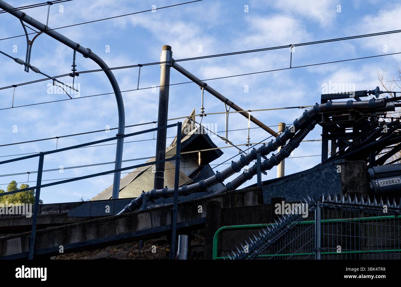 Linee elettriche aggrovigliate e cavi ferroviari fanno da cornice al tetto di una tradizionale torre dell'orologio nella periferia di Tokyo Foto Stock