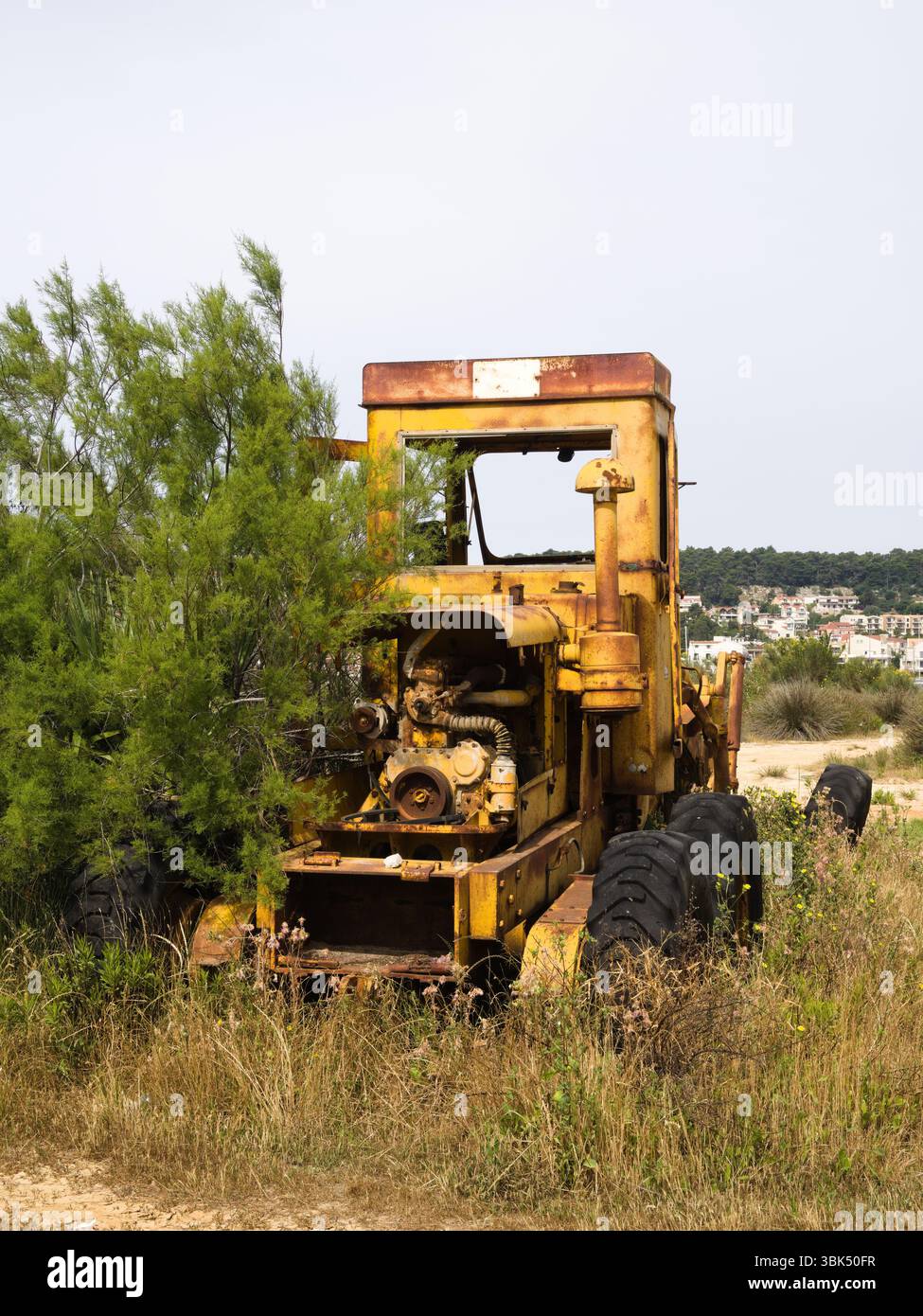 Trattore giallo arrugginito in decomposizione nel campo rurale asciutto accanto alla prateria asciutta Foto Stock