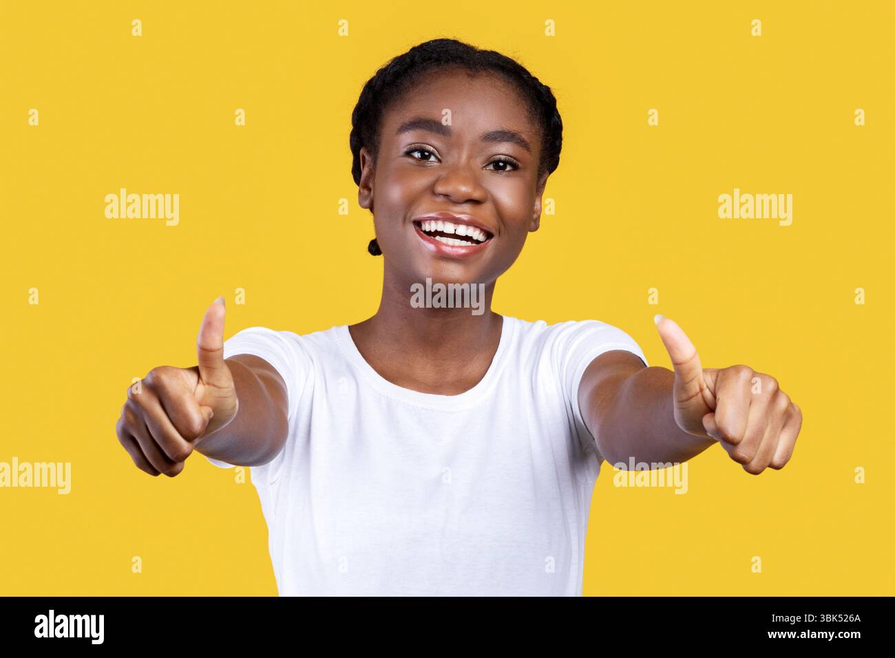 Donna africana gesturing Thumbs-Up con entrambe le mani su sfondo giallo Foto Stock