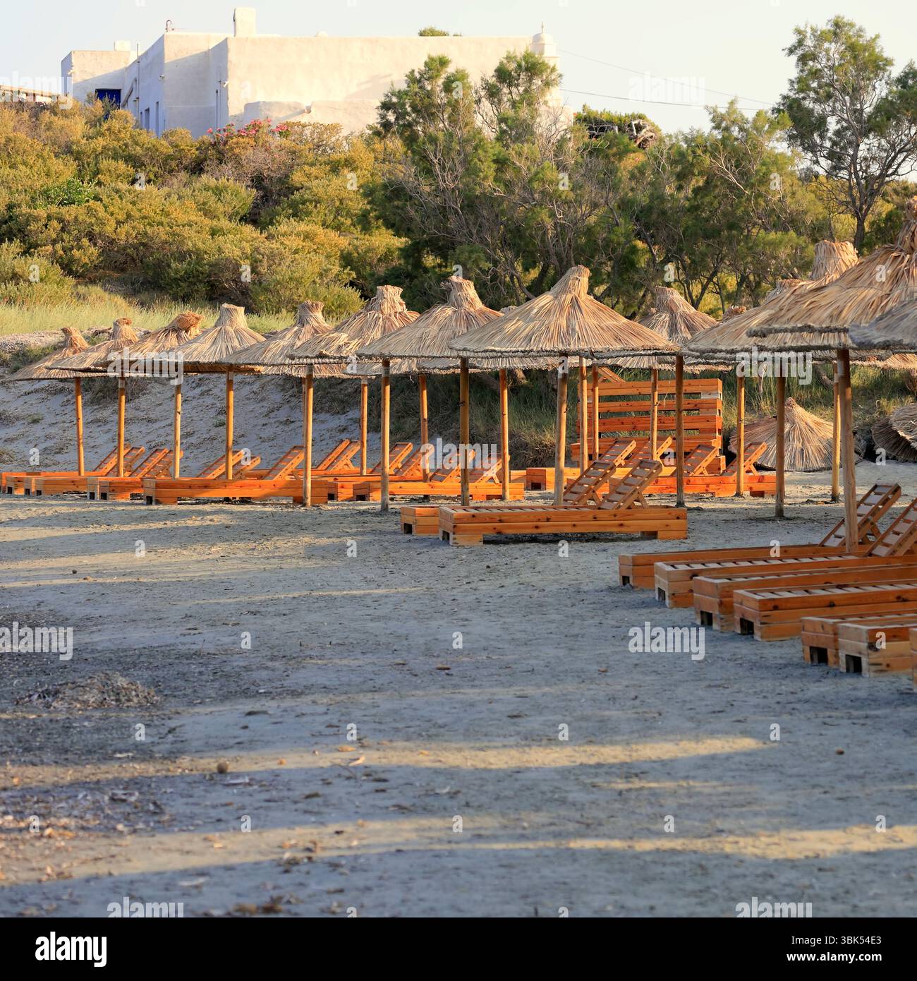 Lettini in legno e ombrelloni di paglia, Tinos, il gruppo delle isole Cicladi, Grecia. Preso l'estate del 2025 giugno Foto Stock