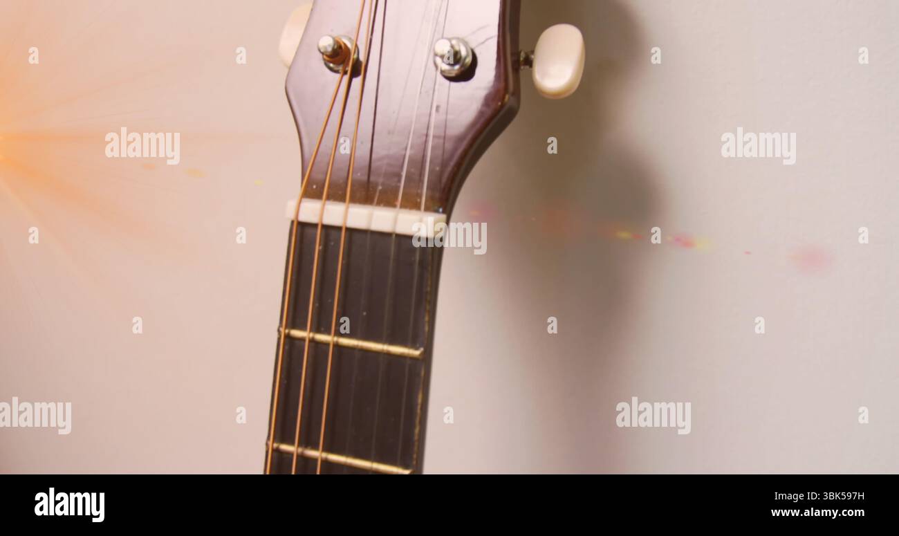 Mostra la testa della chitarra acustica appoggiata contro la parete, con piedini di sintonizzazione, corde e bagliore della lente Foto Stock