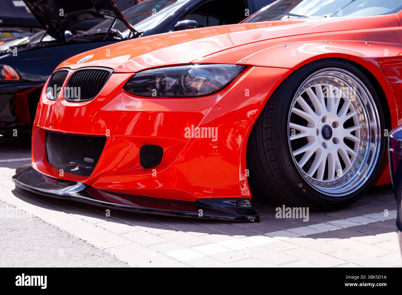 Vilnius, Lituania - 31-05-2025 - BMW serie 3 rossa con kit carrozzeria personalizzato abbassato, campanatura negativa aggressiva e ruote cromate a labbro profondo Foto Stock