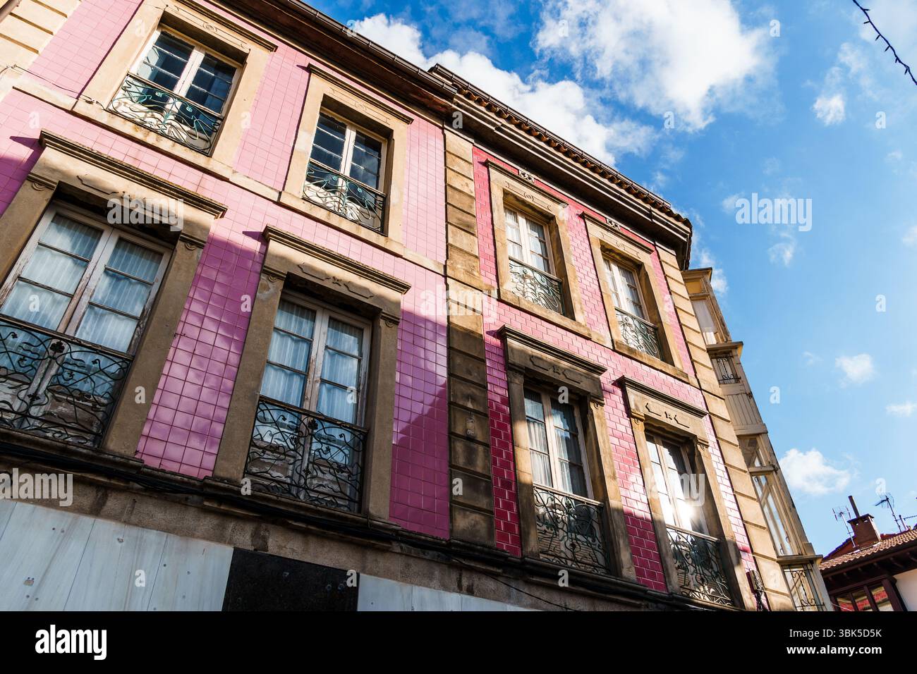 Edificio piastrellato di rosa con finestre multiple e balconi sotto un cielo luminoso. Villaviciosa, Asturie Foto Stock