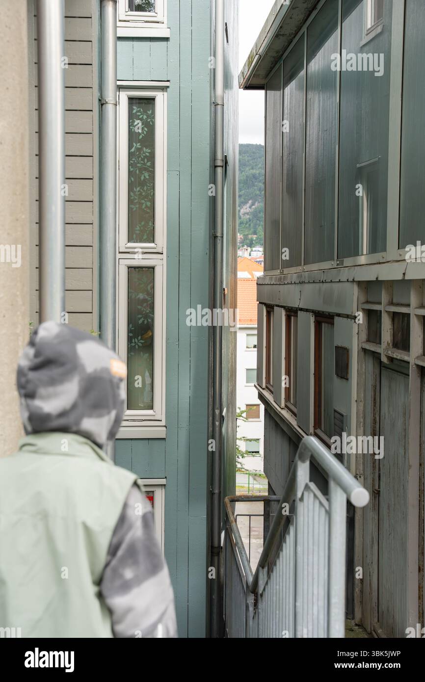 Bambino in giacca con cappuccio che esplora i vicoli stretti tra edifici in legno a Bergen Foto Stock