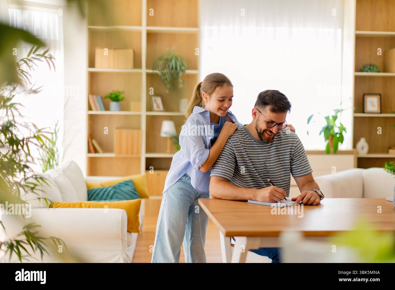 Un padre ama trascorrere un po' di tempo con sua figlia mentre si dedicano alle attività di scrittura in un soggiorno splendidamente progettato con luce naturale. Foto Stock
