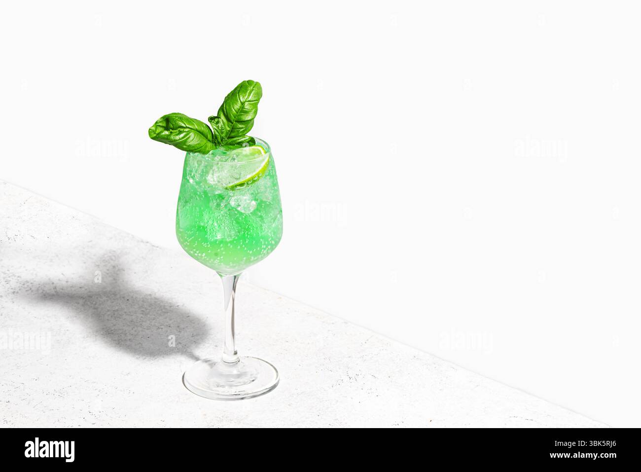Cocktail con pappagallo verde su sfondo bianco, spazio di copia. Gin Basil Smash drink con cubetti di ghiaccio. Rinfrescante mocktail al basilico estivo. Foto Stock