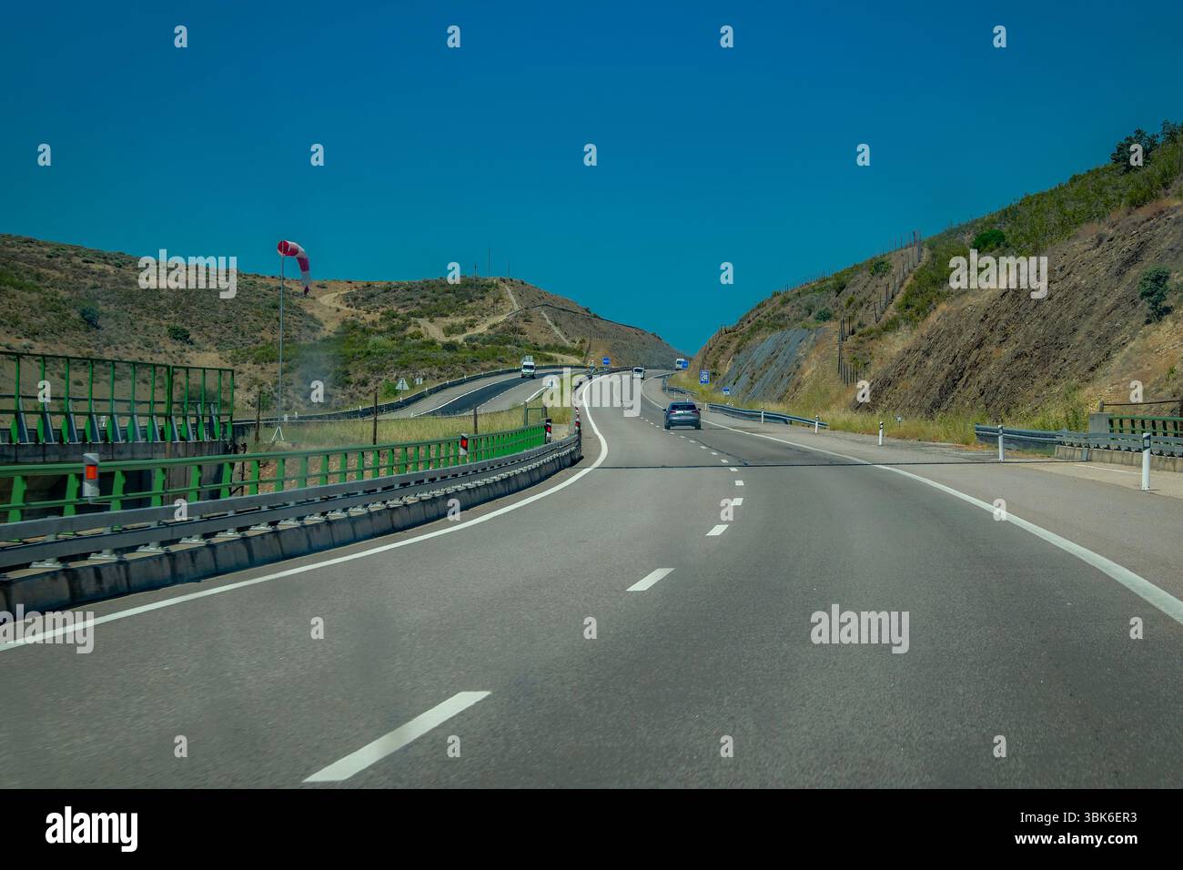 Ripresa a livello degli occhi di una strada pulita e curvilinea che conduce attraverso terreni collinari sotto un cielo luminoso. Foto Stock