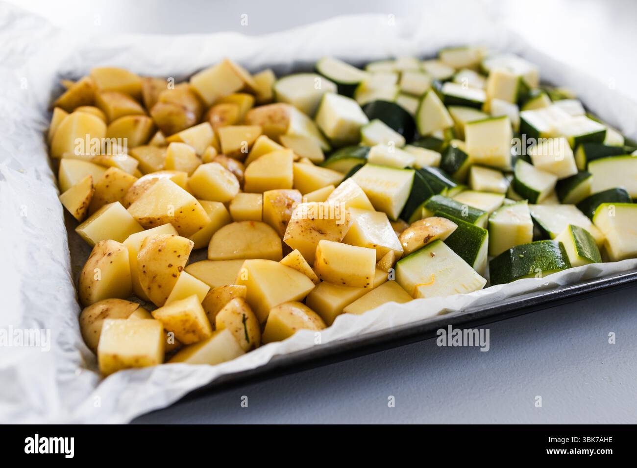patate novelle tritate e zucchine a cubetti su un vassoio da forno, preparate per la tostatura in un semplice piatto fatto in casa Foto Stock patate novelle tritate e zucchine a cubetti su un vassoio da forno, preparate per la tostatura in un semplice piatto fatto in casa Foto Stock