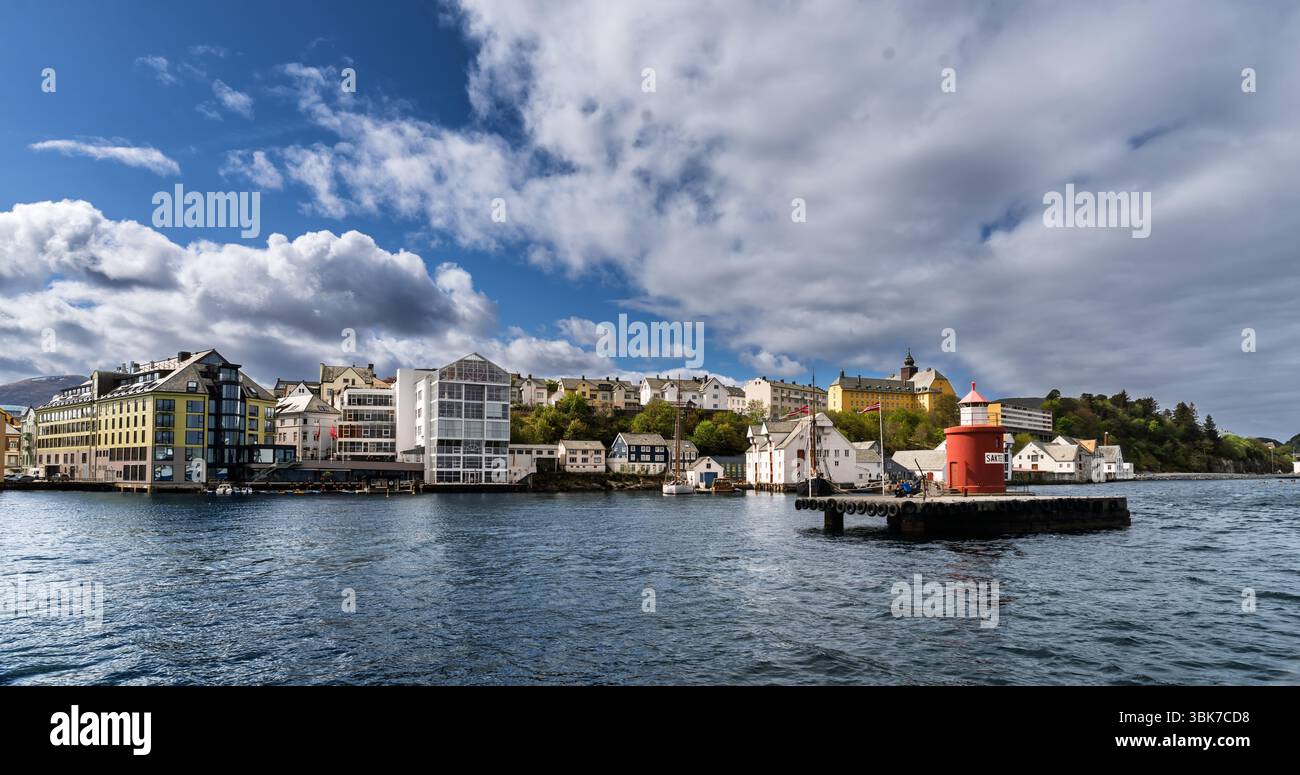 Vista pittoresca di una città costiera con edifici colorati vicino all'acqua, un faro prominente e un cielo blu nuvoloso sullo sfondo, che evoca tran Foto Stock