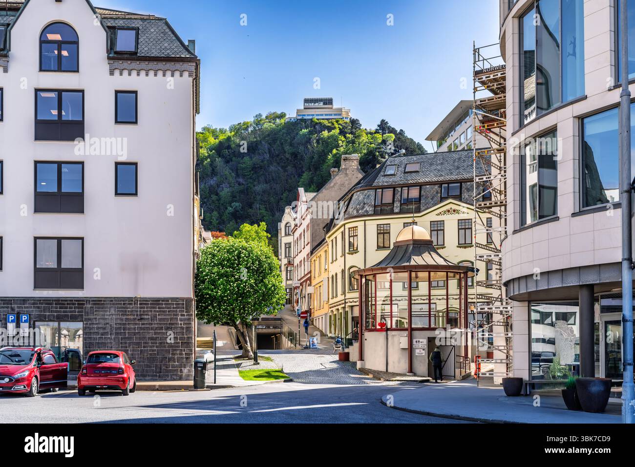 Una vista di un'affascinante strada urbana con architettura storica, vegetazione circostante e veicoli parcheggiati sotto un cielo blu brillante. Una fusione di vita urbana Foto Stock