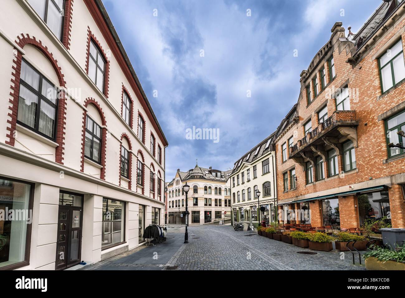 Un'affascinante strada urbana caratterizzata da pavimentazione di ciottoli, architettura storica, caffetterie all'aperto e un cielo nuvoloso, che presenta un'atmosfera da città europea e. Foto Stock
