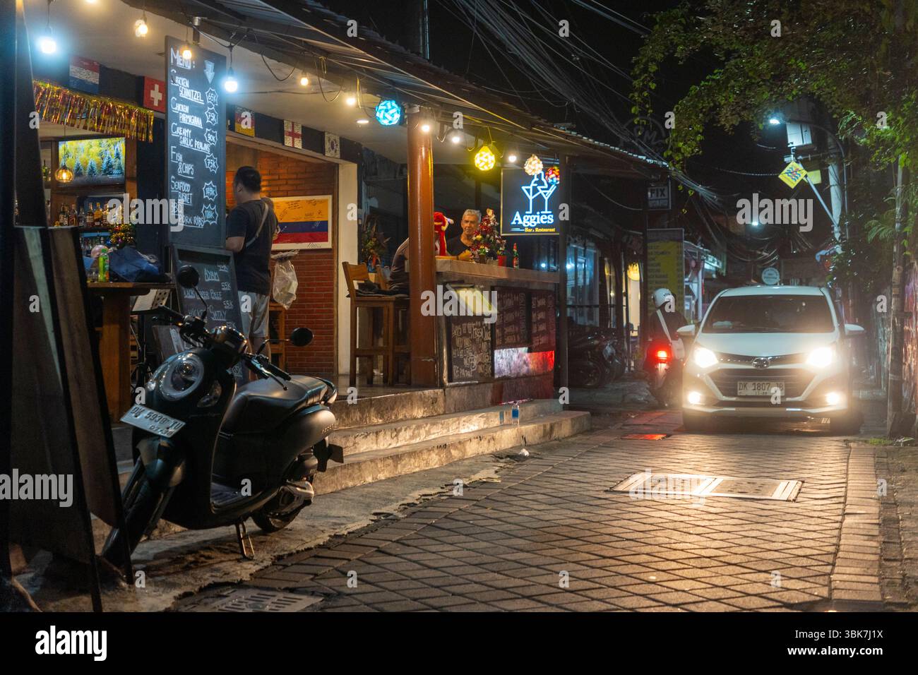 Bali, Indonesia - 25 dicembre 2024: Vicolo scuro con un cartello Aggies appeso sopra di esso a Kuta, Bali. La strada è vuota e tranquilla, con solo pochi parcheggiati Foto Stock