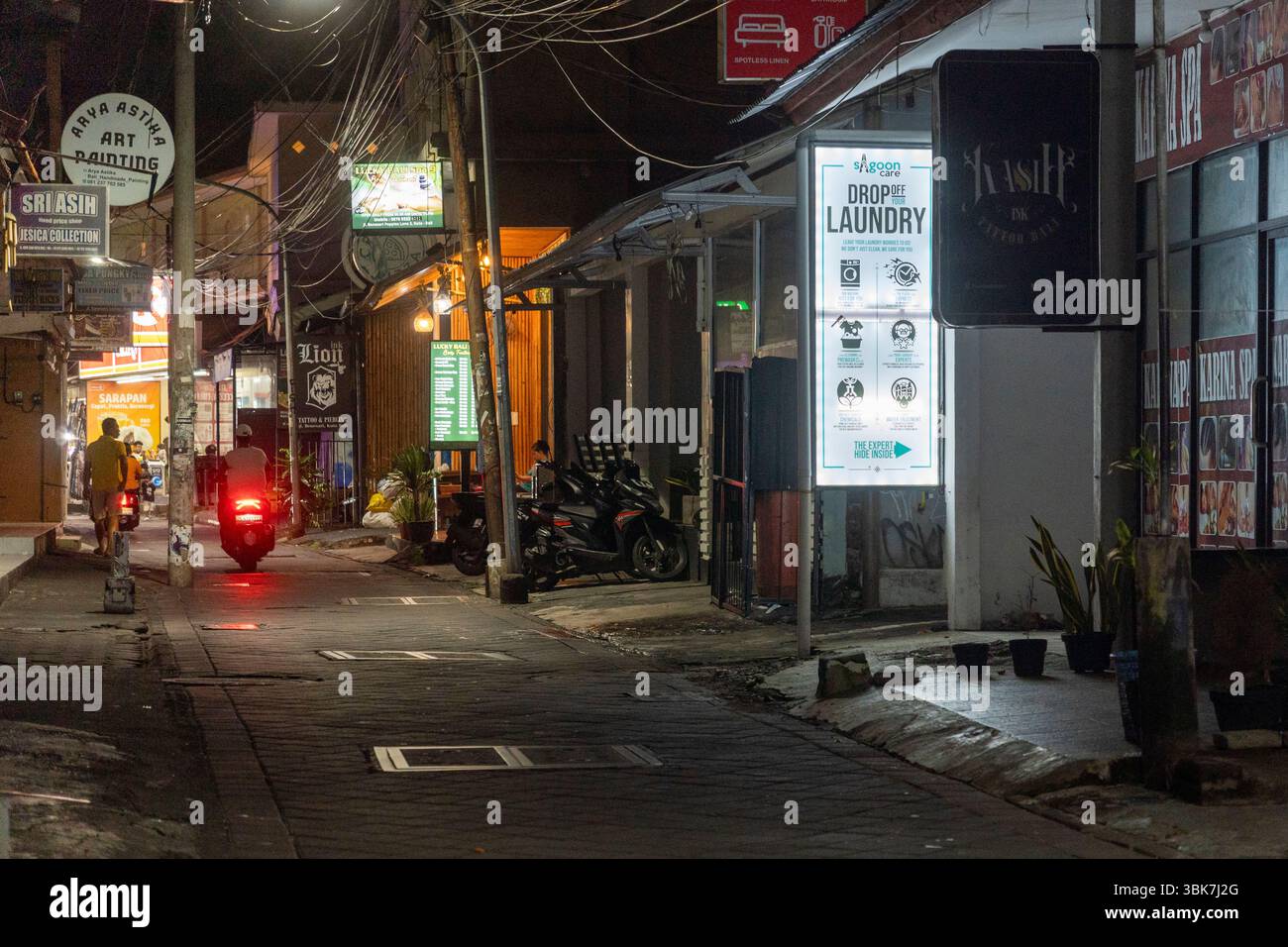 Bali, Indonesia - 25 dicembre 2024: Vicolo buio con un cartello di lavanderia appeso sopra di esso a Kuta, Bali. La strada è vuota e tranquilla, con solo pochi parcheggi Foto Stock