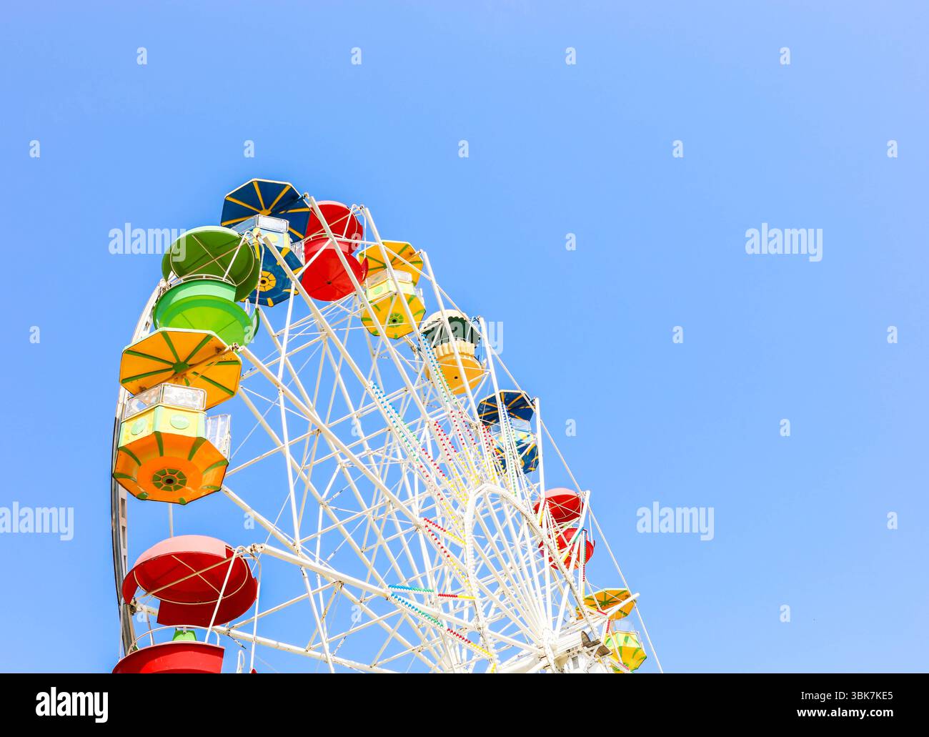 La variopinta ruota panoramica con gondole luminose è esposta in modo prominente contro un cielo azzurro, evidenziando l'atmosfera giocosa e l'emozione di un Foto Stock