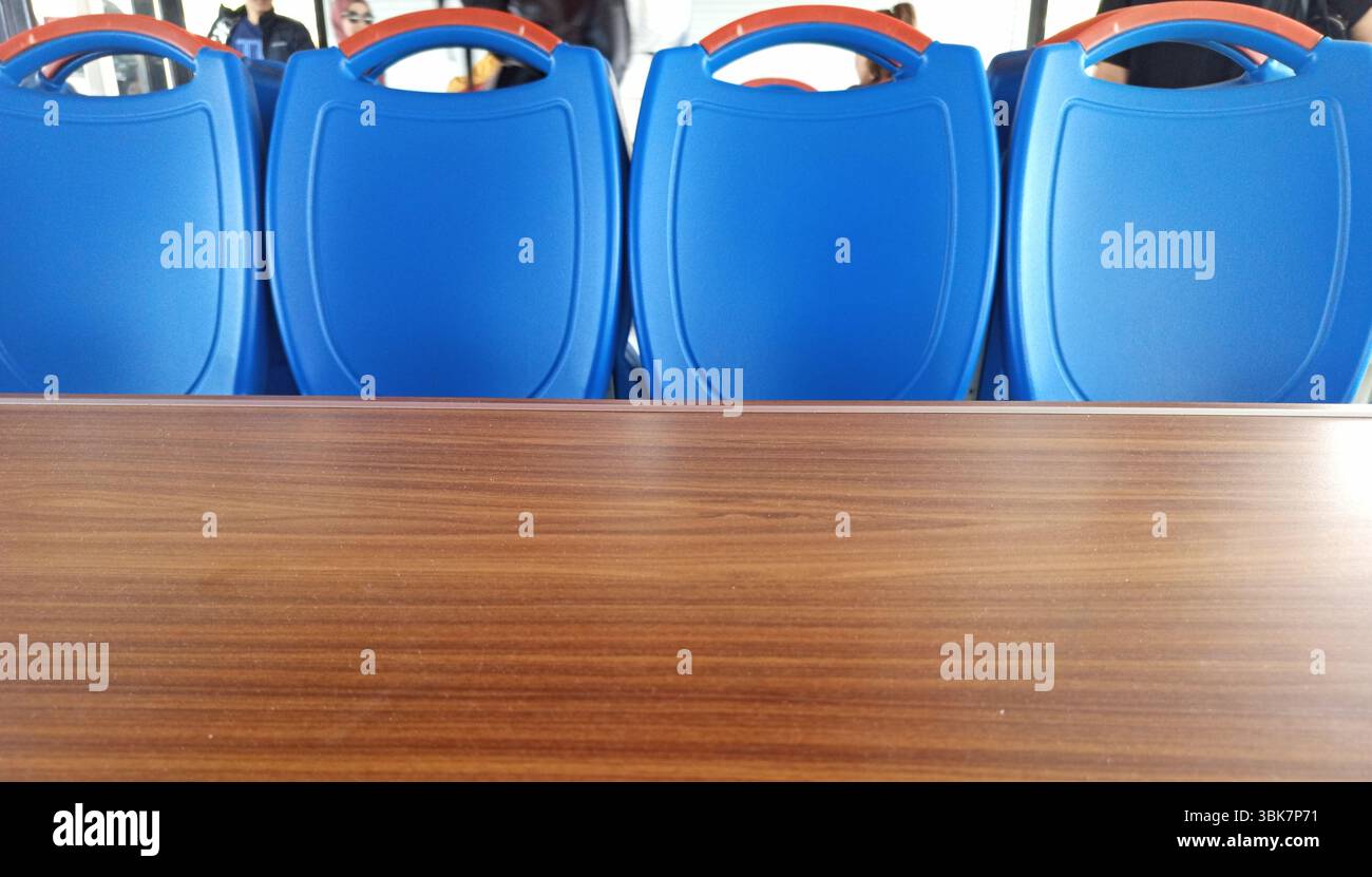Quattro vivaci sedie blu sono allineate ordinatamente davanti ad un tavolo in legno lucido, creando uno spazio pulito e invitante. Lo sfondo suggerisce un vivace Foto Stock
