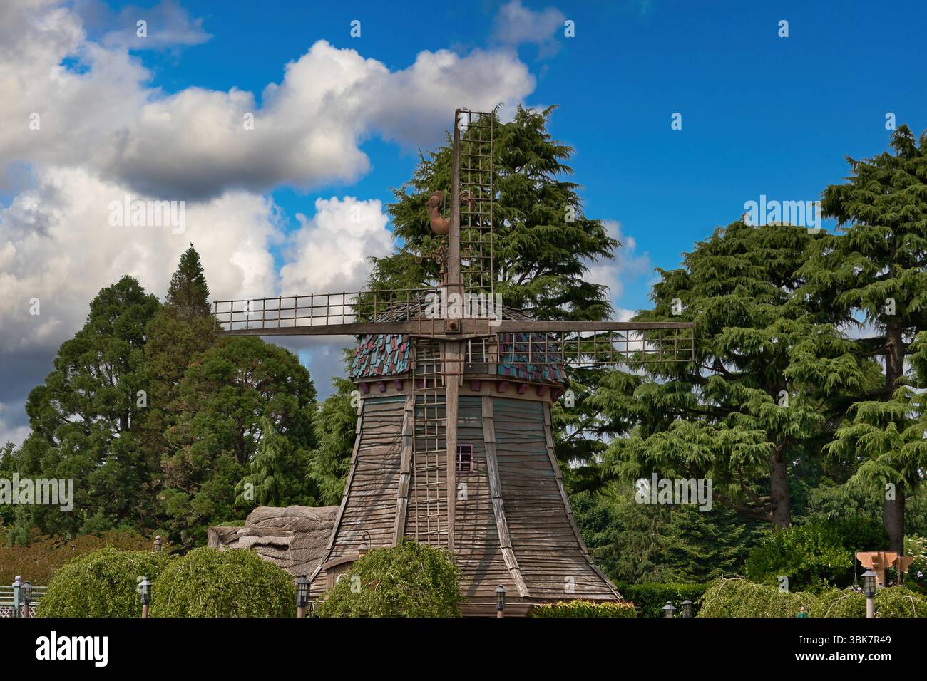 Un mulino a vento sorge in mezzo a una lussureggiante vegetazione sotto un cielo parzialmente nuvoloso, con il suo legno intemprato e il tetto colorato che aggiunge interesse visivo a Disneyland Paris Foto Stock