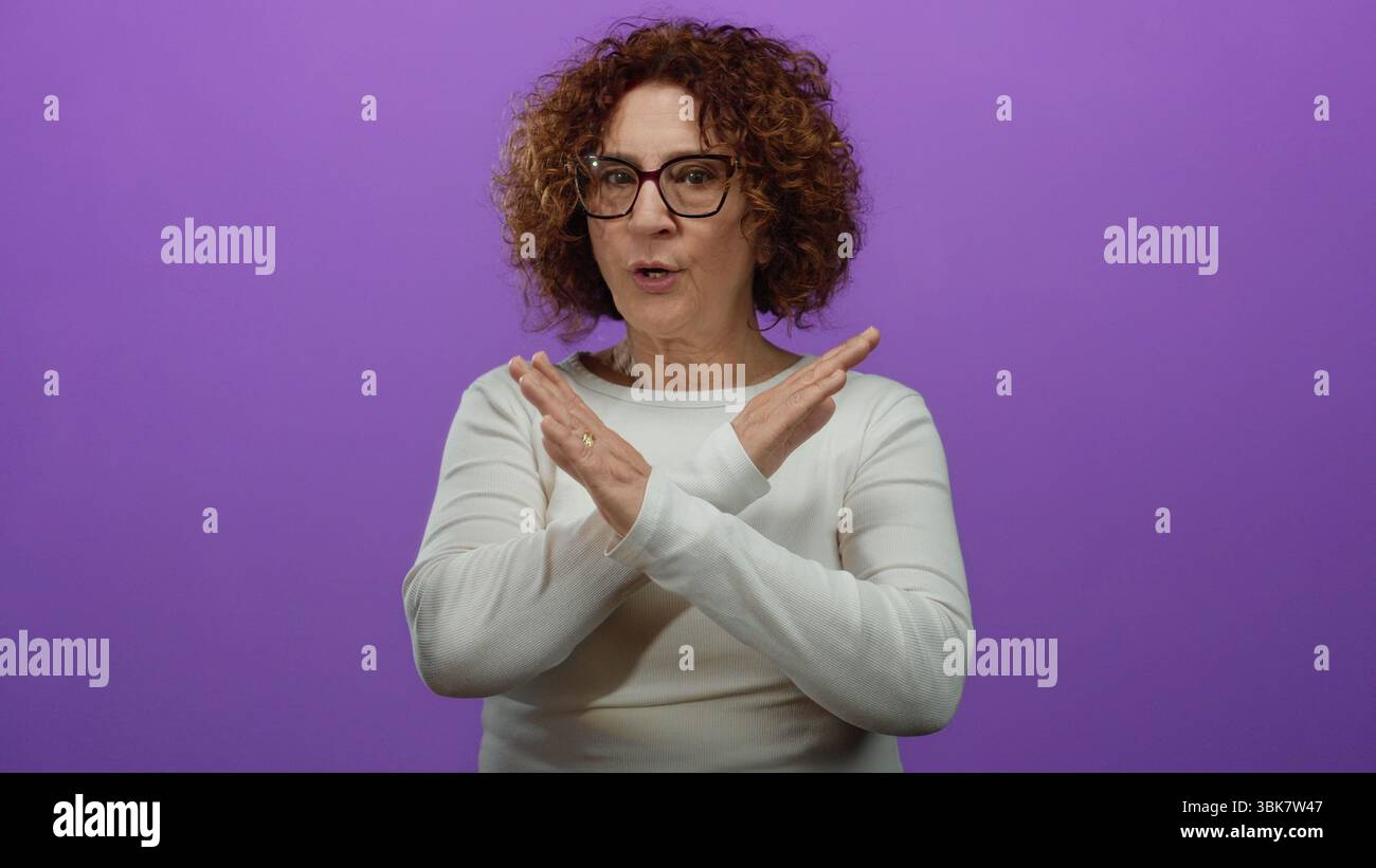 La donna ispanica di mezza età si ferma in una parte superiore bianca su uno sfondo viola isolato. Foto Stock