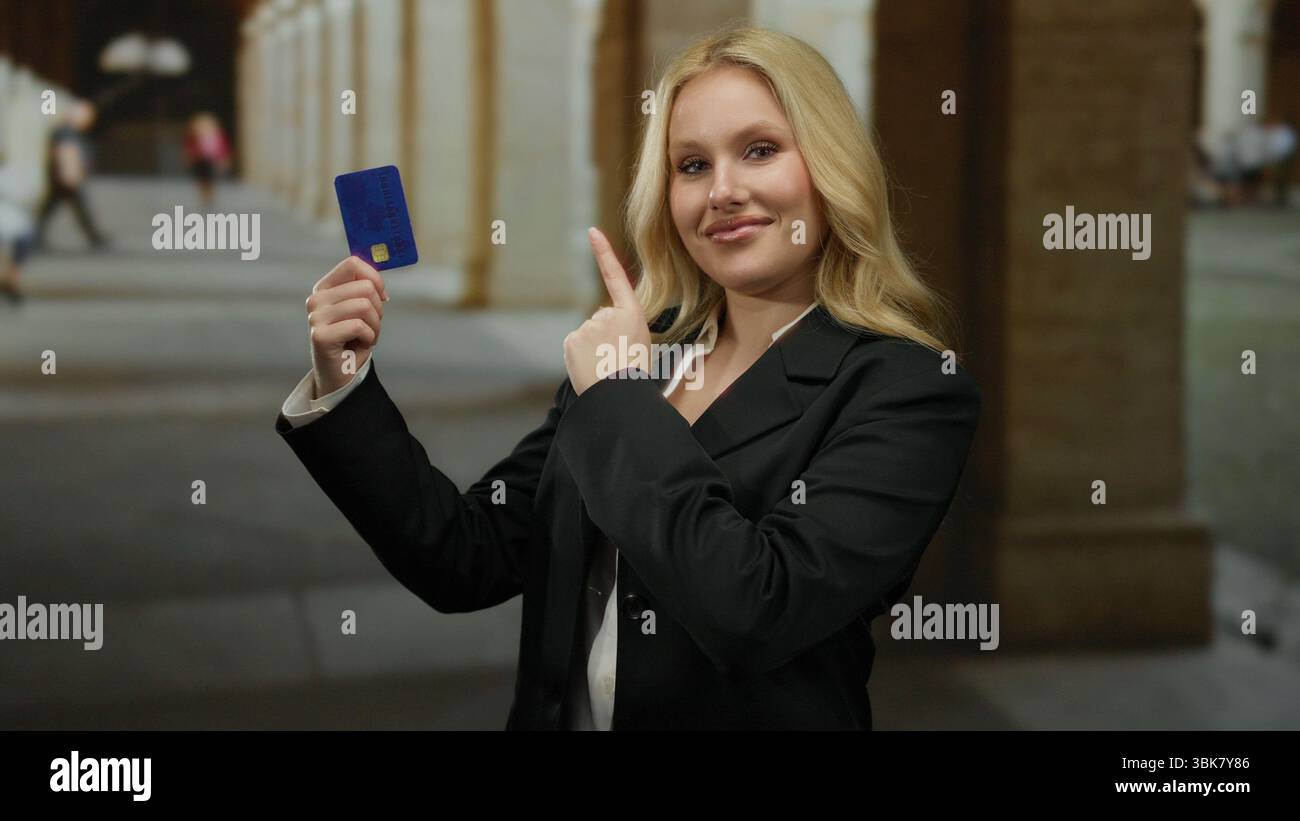 Donna che mostra la carta di credito nel corridoio del campus universitario, trasuda fiducia e stile, circondata da architettura storica, incarna un'educazione moderna Foto Stock