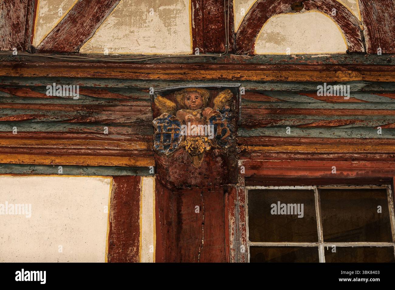 Dipingi le bucce di un angelo scolpito con ali e capelli dorati, fiancheggiate da croci cristiane, mentre guarda in basso impassibile da una placca di legno sulla facciata intemprata e fatiscente di una delle tante antiche case in legno a graticcio nell'Altstadt o nel centro storico di Limburg an der Lahn in Assia, Germania. Foto Stock
