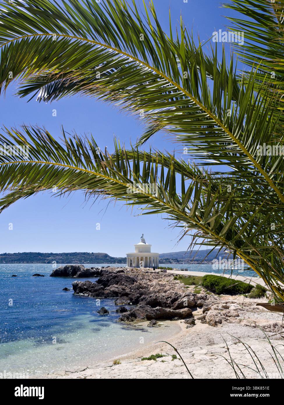 Faro bianco con colonne sulla costa rocciosa di Cefalonia, incorniciato da foglie di palma e mare turchese. Foto Stock