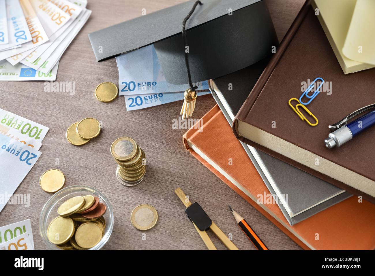Concetto di spesa per l'istruzione con bacheca su una pila di libri e denaro su una tavola di legno. Vista dall'alto. Foto Stock